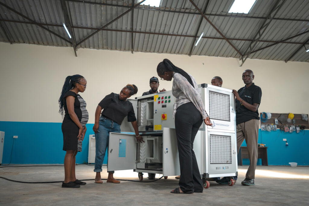 2023 Rolex Awards for Enterprise Laureate Beth Koigi explaining the technical details of an atmospheric water generator to her team in a Majik Water warehouse. Majik Water is led entirely by women and installs these machines in arid and semi-arid regions where they extract clean, mineralised water from thin air