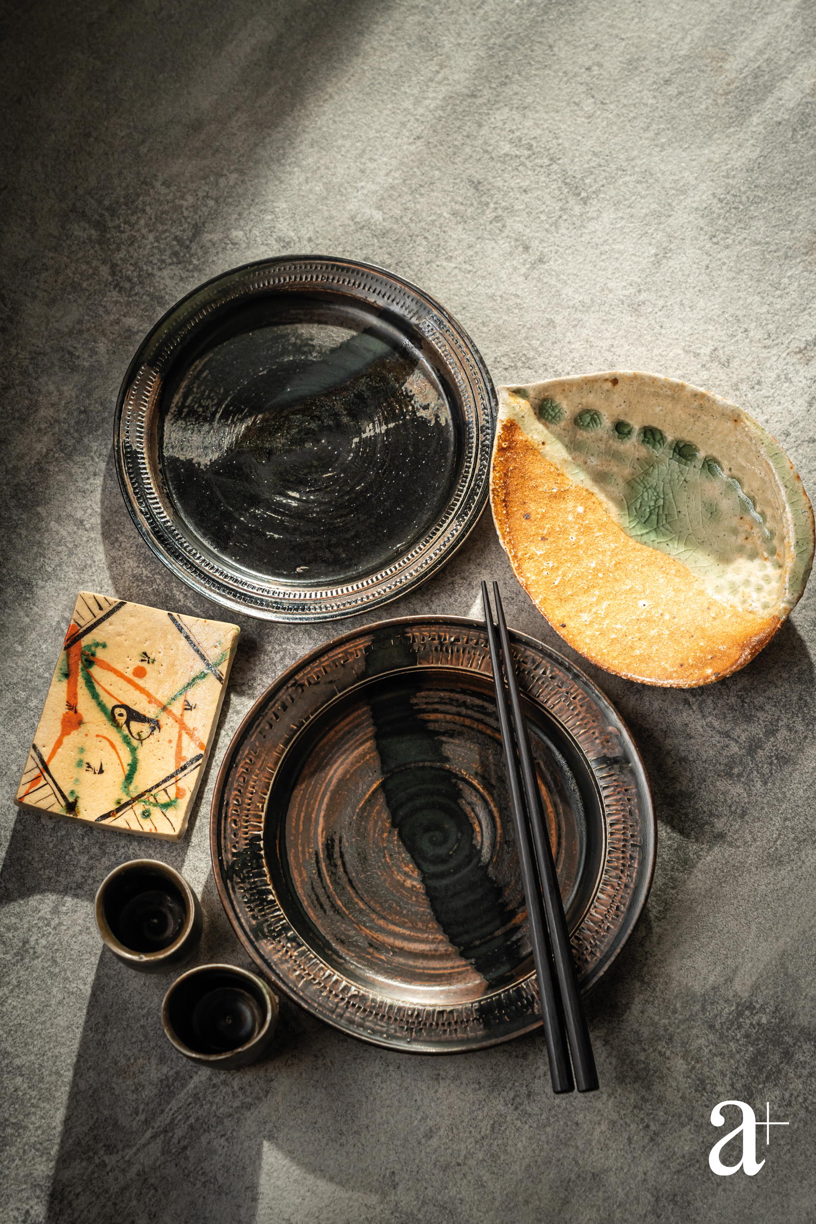 Clockwise from top: Kuro Karatsu Hirazara by Yukiko Tsuchiya; Shigaraki Awabi Mukozuke Plate by Katsunori Sawa; Kuro Karatsu Hirazara and sake cups by Yukiko Tsuchiya; and Yashichida-Oribe Square Plate by Katsunori Sawa (Credit: Yvonne Isabelle Ling)