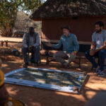 Boyes and Costa discussing water use with Angolan kings and chiefs from communities along the Zambezi. In front of them is a map of Central Africa (Credit: Rolex/Aurélie Marrier d’Unienville)